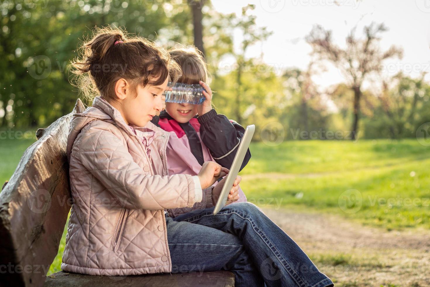 photo de deux petites filles à l'aide d'une tablette sur le banc