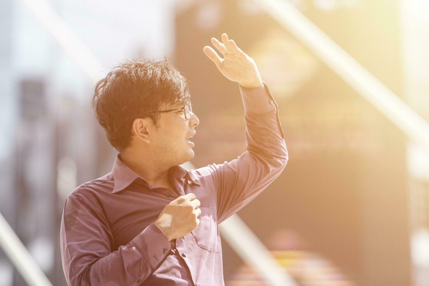 homme d'affaires asiatique violet avec t-shirt sous le soleil se cachant à la main sur fond de ville moderne flou. photo