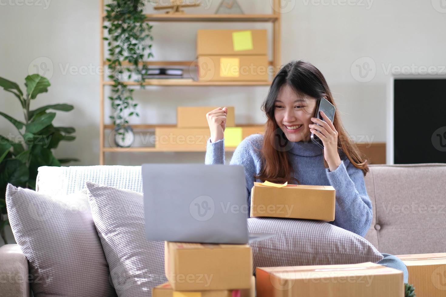 heureuse jeune femme entrepreneure asiatique, sourire pour le succès des ventes après avoir vérifié la commande du magasin d'achat en ligne dans un smartphone au bureau à domicile, concept d'entreprise marchande en ligne et de commerce électronique photo