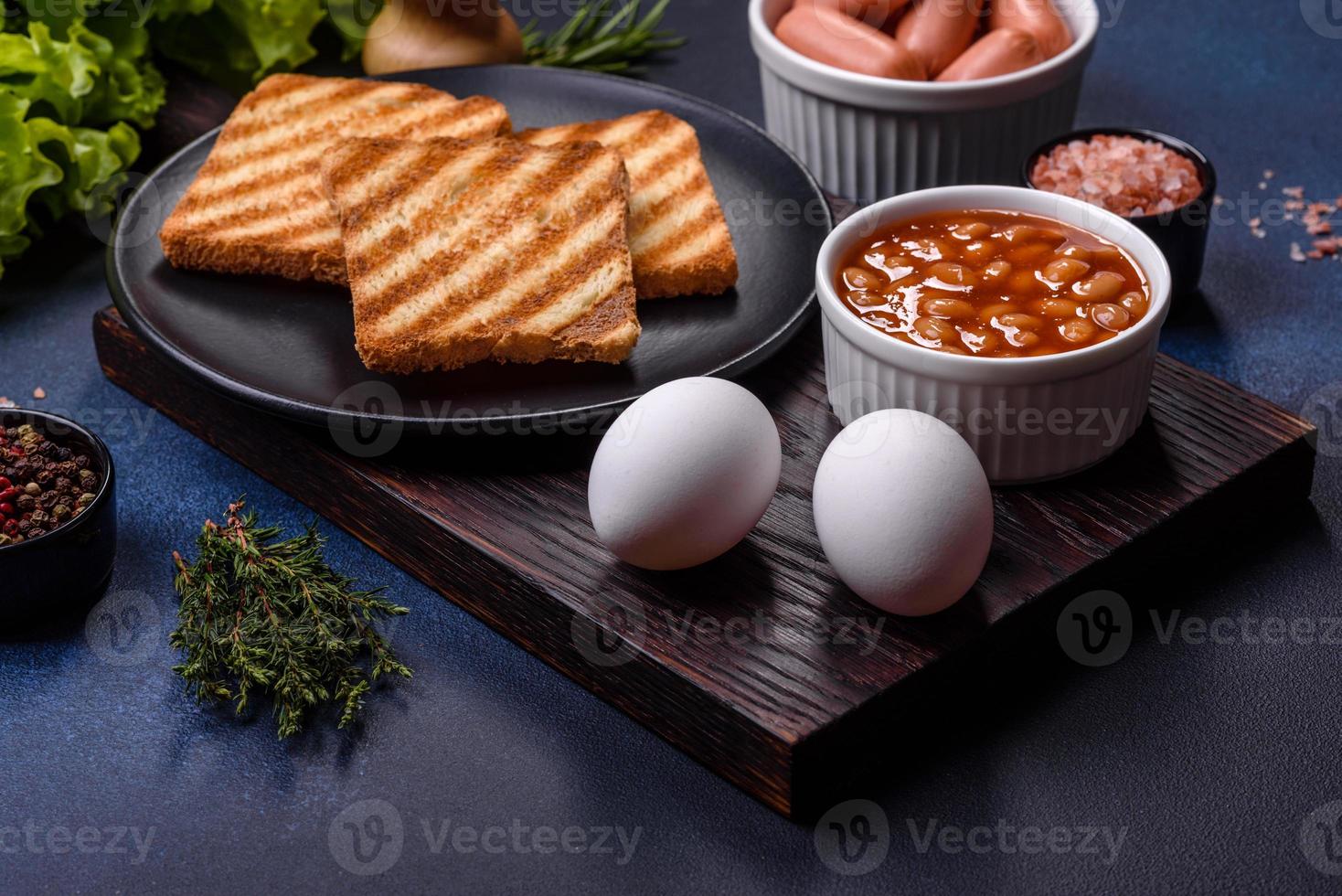 petit-déjeuner anglais traditionnel avec œufs, pain grillé, saucisses, haricots, épices et herbes sur une plaque en céramique grise photo