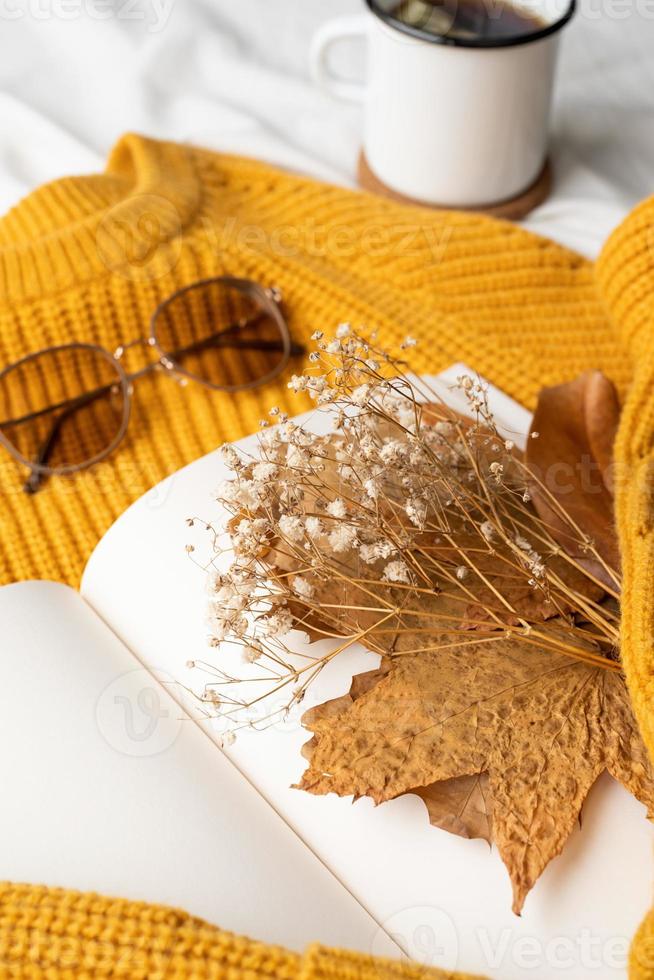 composition confortable de pull chaud, livre blanc, tasse de thé chaud et feuilles d'automne photo