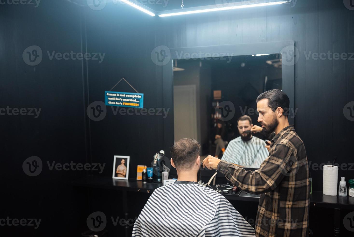 le maître du salon de coiffure fait la coupe de cheveux des hommes avec une tondeuse à cheveux photo