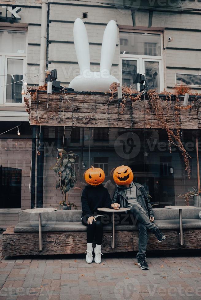 gars et fille avec des têtes de citrouille dans un café de la rue, main dans la main photo