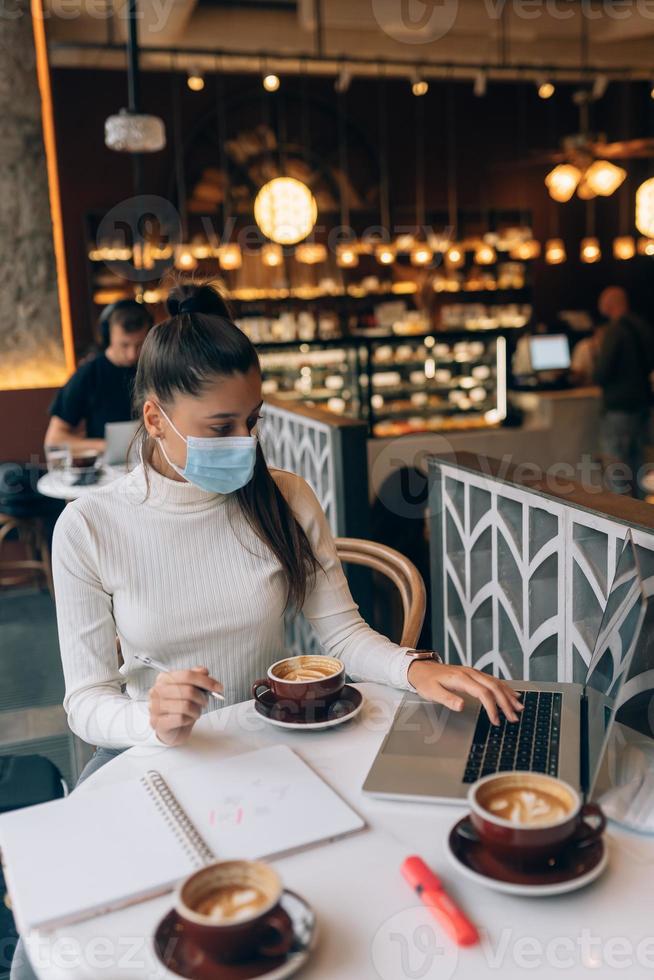 jolie femme portant un masque médical, utilisant un ordinateur portable pour travailler. photo