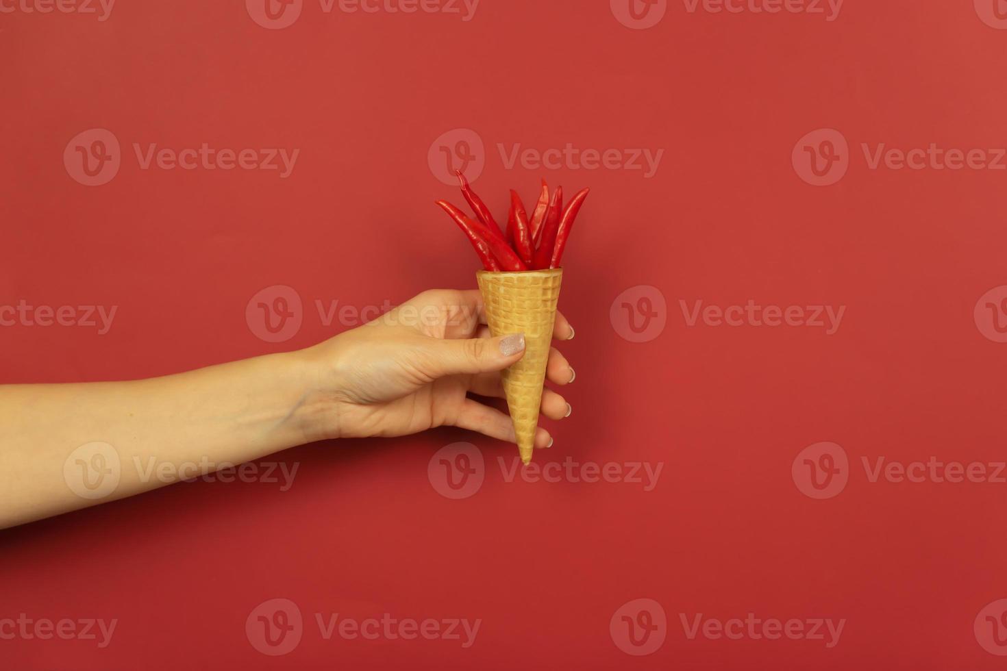 une main de femme tient des mini piments rouges dans le cône gaufré sur fond rouge photo