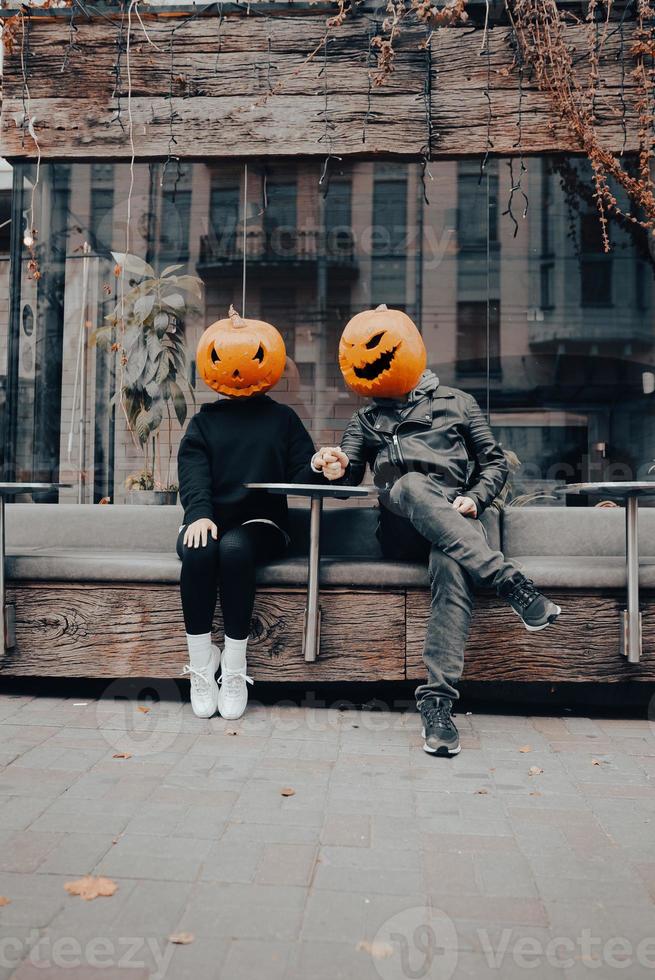 gars et fille avec des têtes de citrouille dans un café de la rue, main dans la main photo