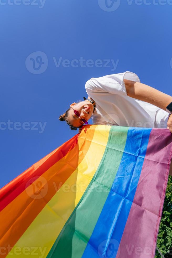 une jeune femme développe un drapeau arc-en-ciel contre le ciel photo