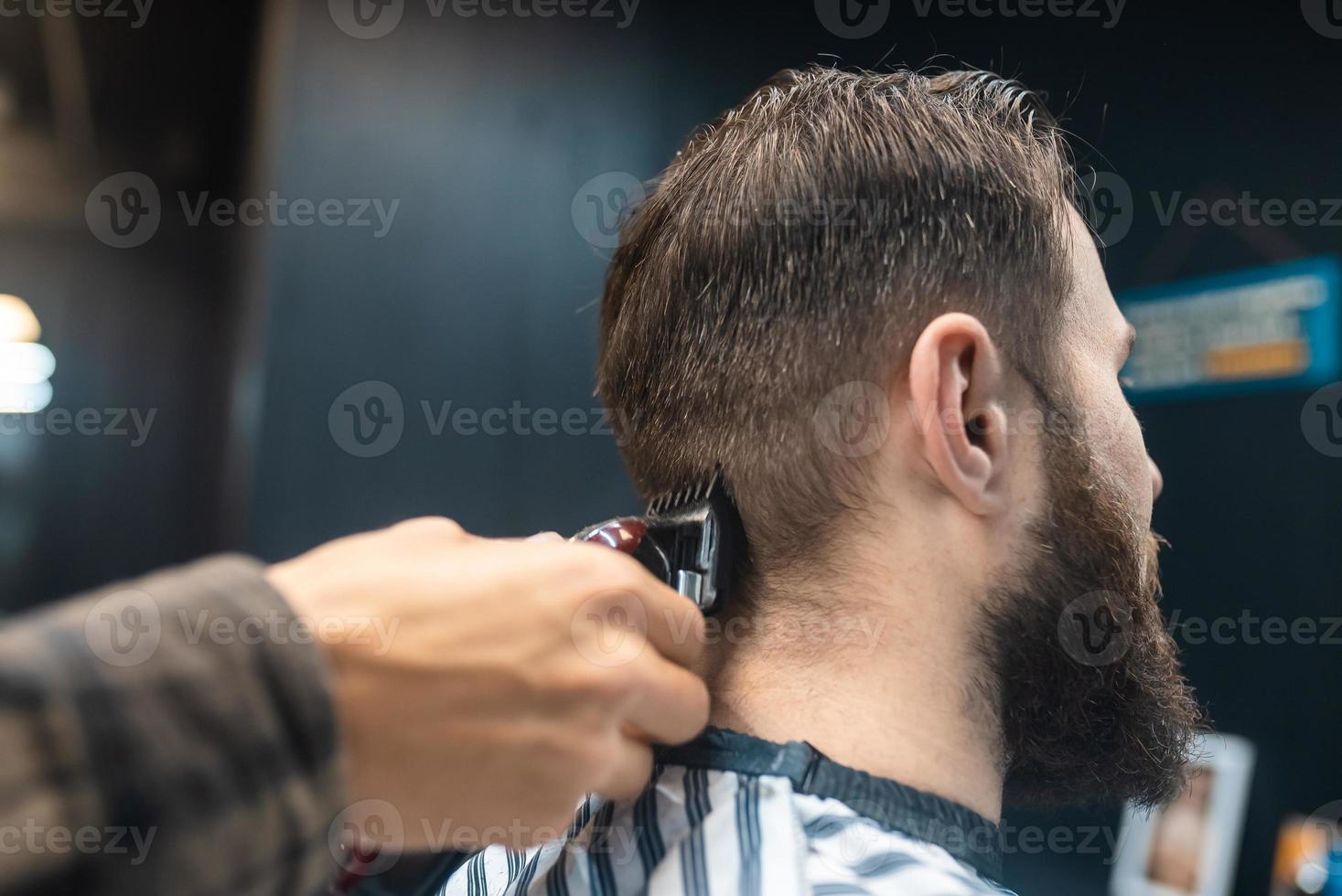 le maître du salon de coiffure fait la coupe de cheveux des hommes avec une tondeuse à cheveux photo