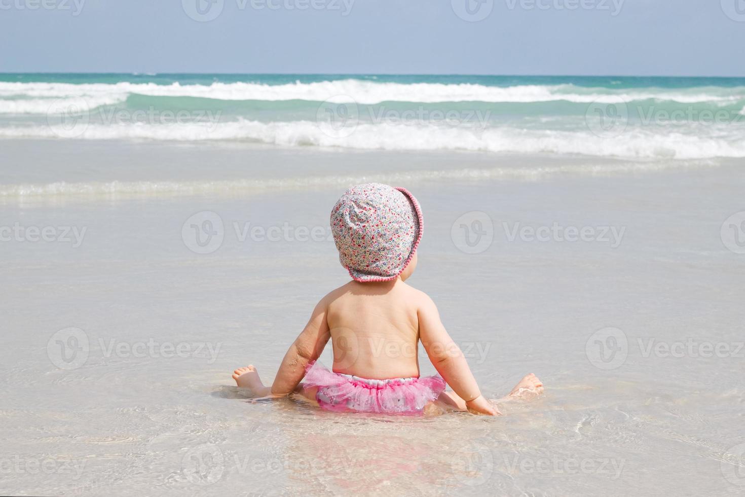 petite fille est assise sur une plage de sable et regarde la mer bleue avec des vagues. photo