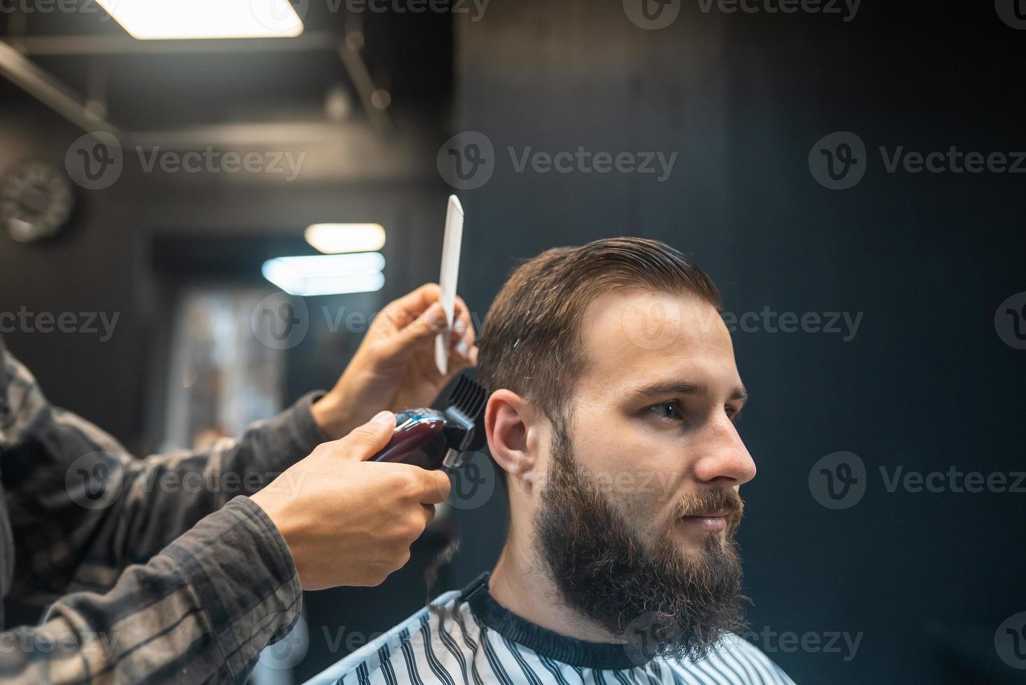 gros plan d'un homme qui se fait couper les cheveux à la mode au salon de  coiffure. coiffeur masculin servant le client, faisant une coupe de cheveux  à l'aide d'une machine et