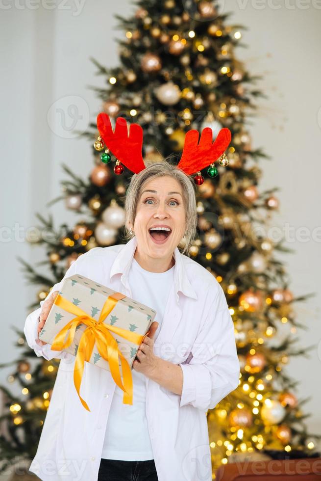 grand-mère portant un chapeau de noël de cerf. cadeau de noël à la main. photo