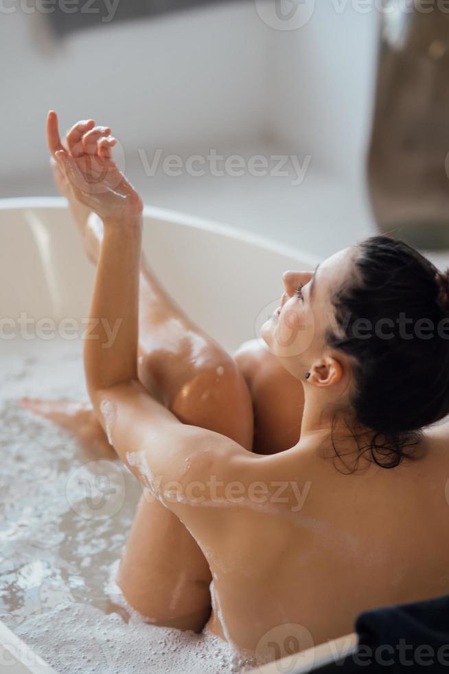 jeune femme étreint ses jambes alors qu'il était assis dans le bain photo