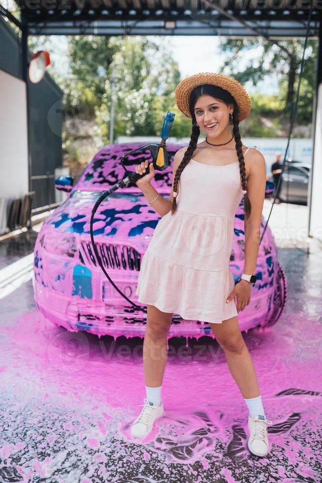 jeune femme flexible se tient devant une voiture recouverte de mousse rose photo