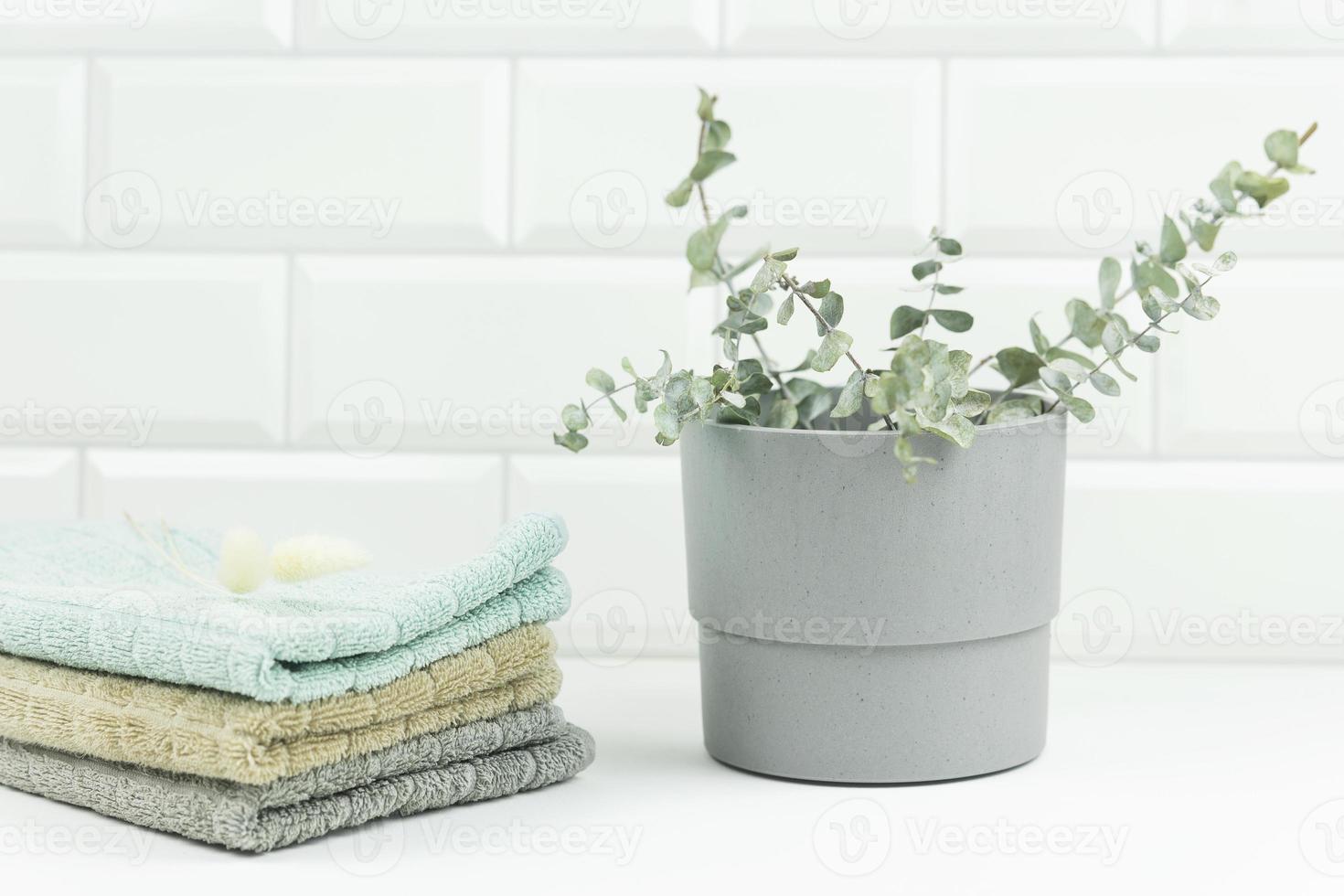 des serviettes en coton de couleur neutre reposent sur une table dans une salle de bains moderne. le pot avec des branches d'eucalyptus se tient à côté d'eux photo