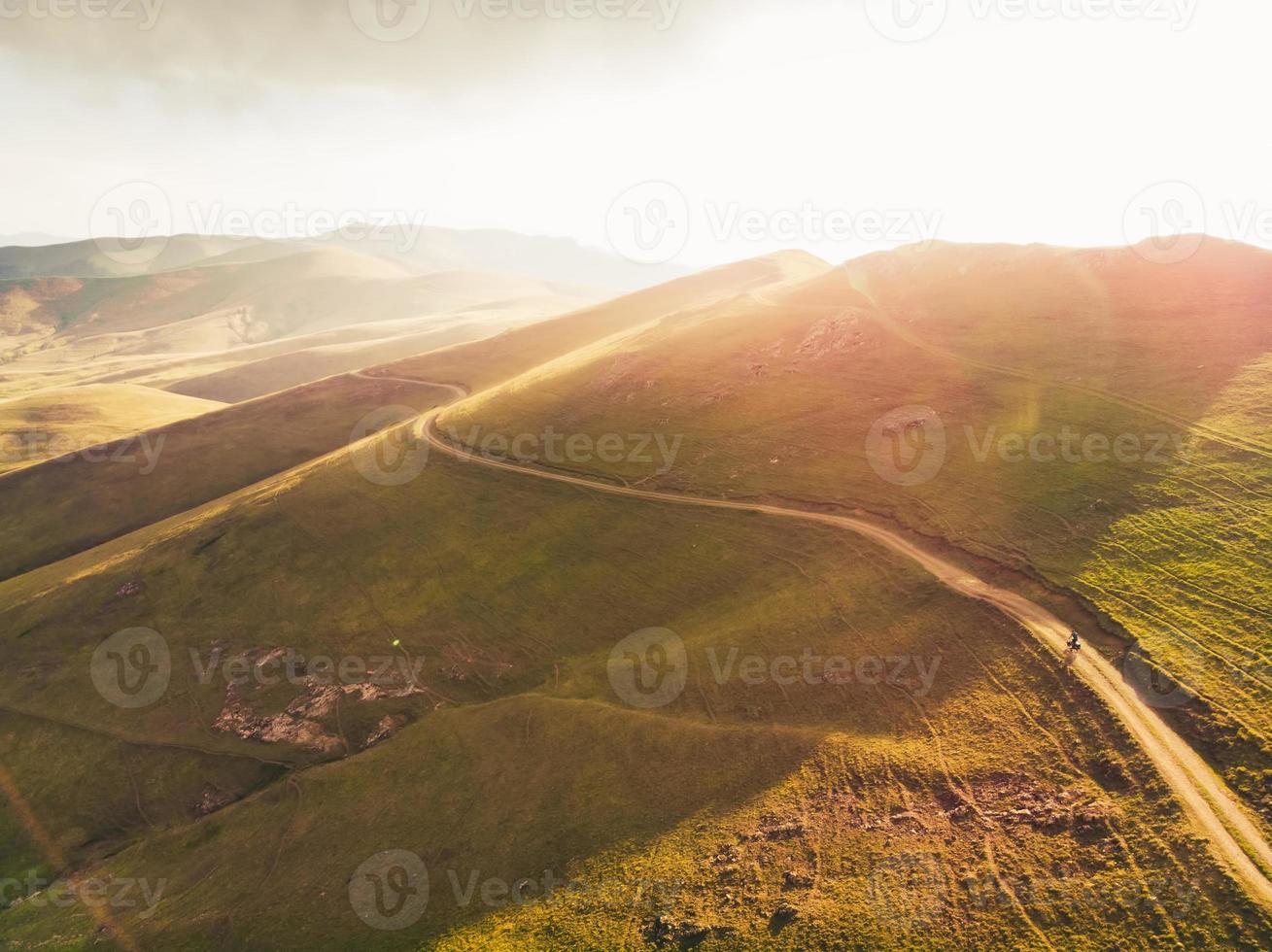 vue aérienne cycliste dans les montagnes de la campagne arménienne pittoresque cyclotourisme à l'extérieur en solo dans un paysage d'été chaud avec fond de ciel lumineux au coucher du soleil. image de cyclisme inspirante photo