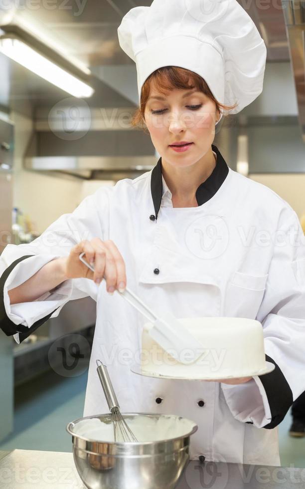chef cuisinier assez concentré finissant un gâteau avec du glaçage photo