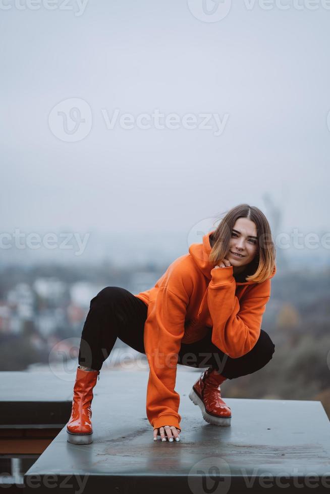 fille dans une veste orange pose sur le toit d'un immeuble du centre-ville photo