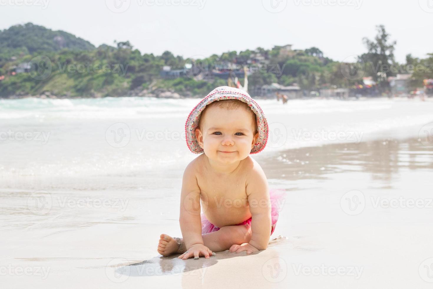 une petite fille souriante joue avec du sable près de la mer sur fond de plage tropicale. photo