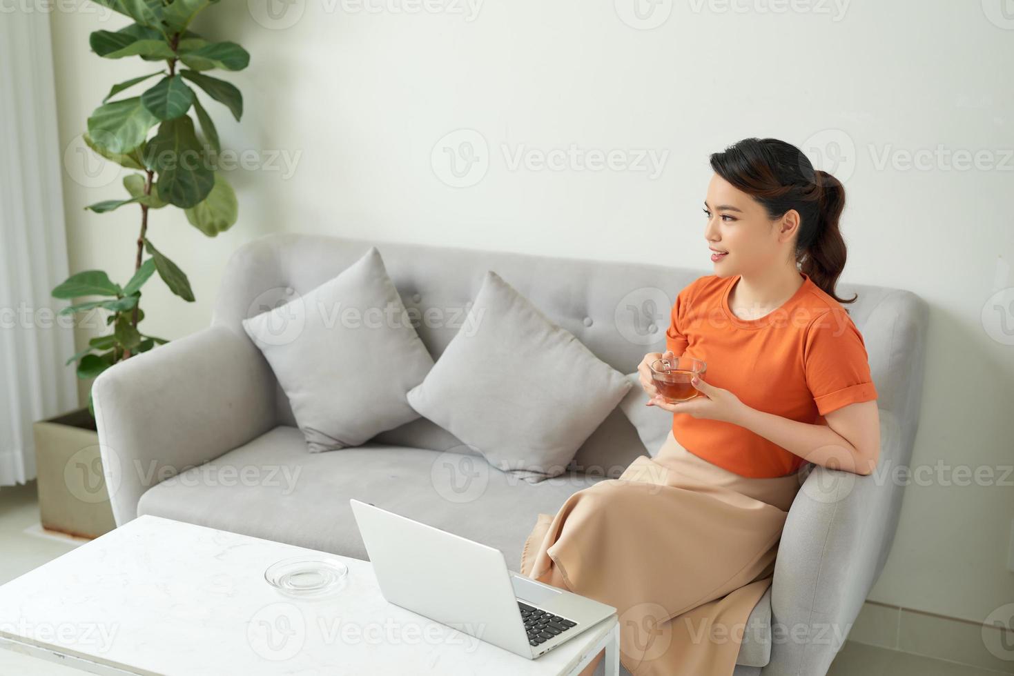 femme asiatique tenant un verre de thé et travaillant sur un ordinateur portable. photo