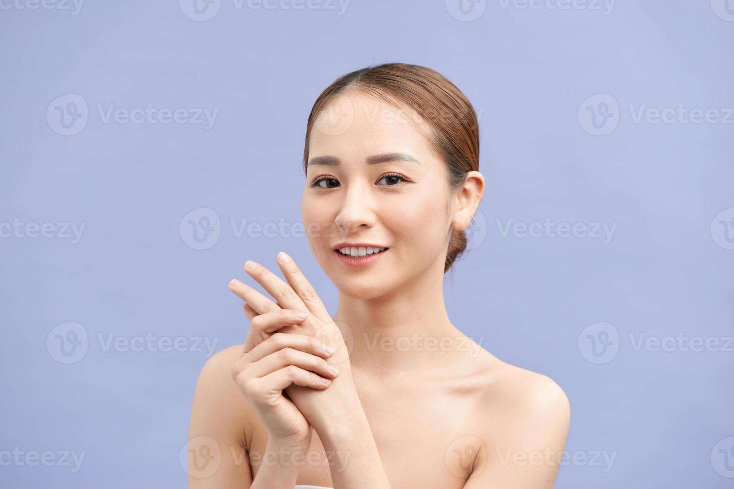 une jeune femme souriante applique de la crème sur ses mains. sur fond violet. photo