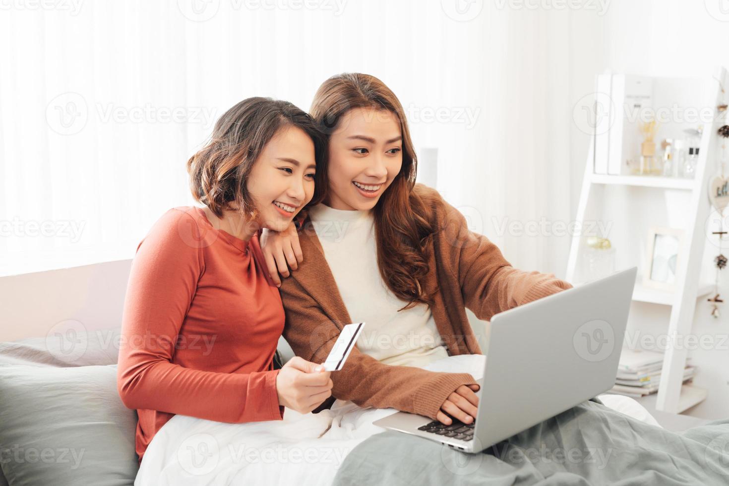 deux amis faisant des achats en ligne avec carte de crédit et ordinateur portable allongé sur le lit à la maison photo