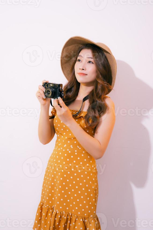 jolie jeune femme touristique en chapeau de robe blanche d'été avec appareil photo isolé sur fond rose.