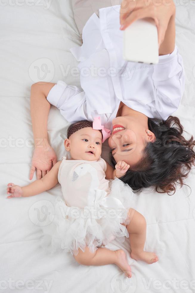 smiley mère et son bébé vous regardant allongé sur le sol à la maison photo
