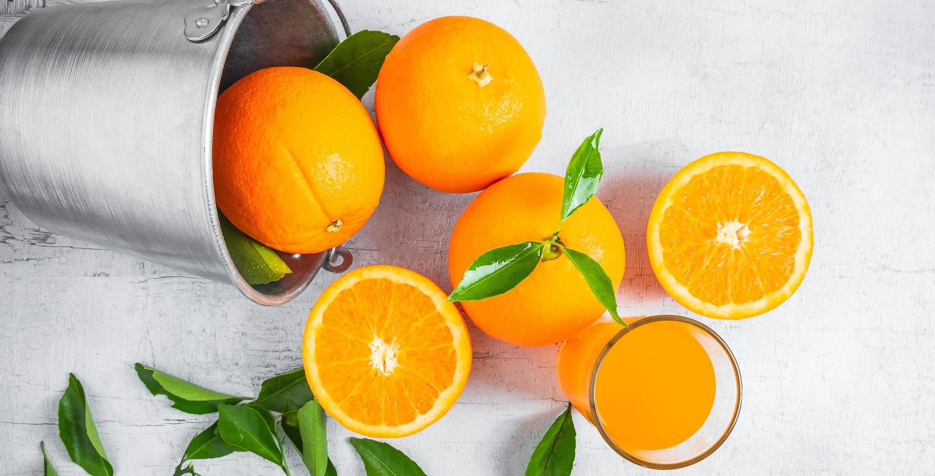 jus d'orange frais et fruits orange sont dans un panier sur un fond en bois blanc. photo