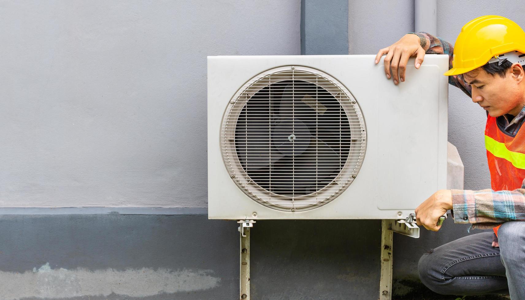 le technicien du climatiseur utilise une clé pour serrer l'écrou du compresseur d'air. réparateur de jeune homme asiatique vérifiant un climatiseur extérieur. photo