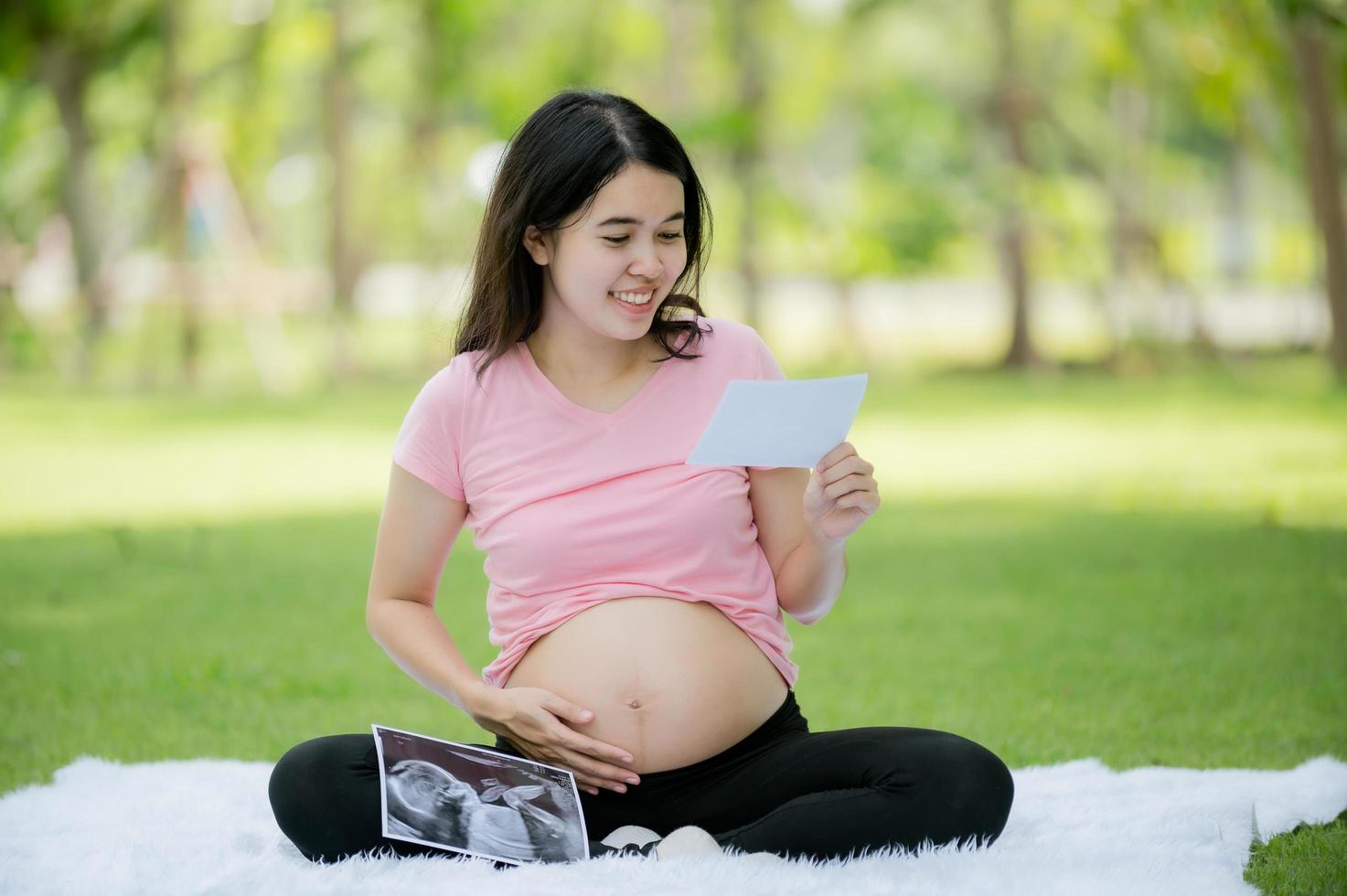 une femme asiatique enceinte pour la première fois est assise dans le jardin en regardant les images de l'échographie de l'hôpital pour vérifier la santé de son bébé en pleine croissance photo