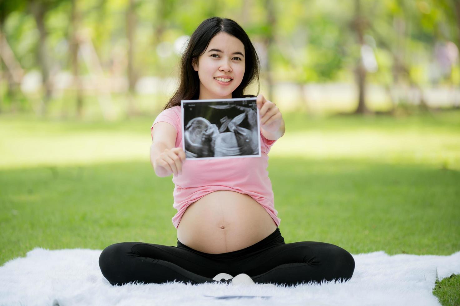 une femme asiatique enceinte pour la première fois s'assoit et se détend pour montrer ses images d'une échographie hospitalière pour vérifier la santé de son bébé en pleine croissance photo