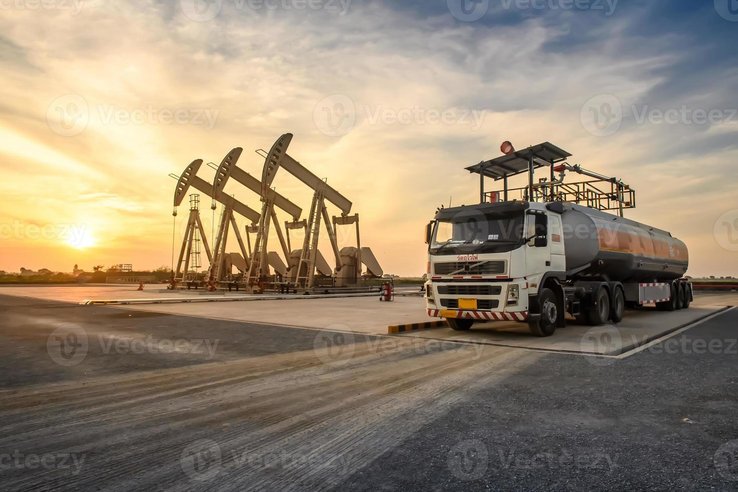 les plates-formes pétrolières et les camions pétroliers fonctionnent ou sont garés pour drainer le pétrole dans les champs pétrolifères. au coucher ou au lever du soleil le soir ou le matin photo