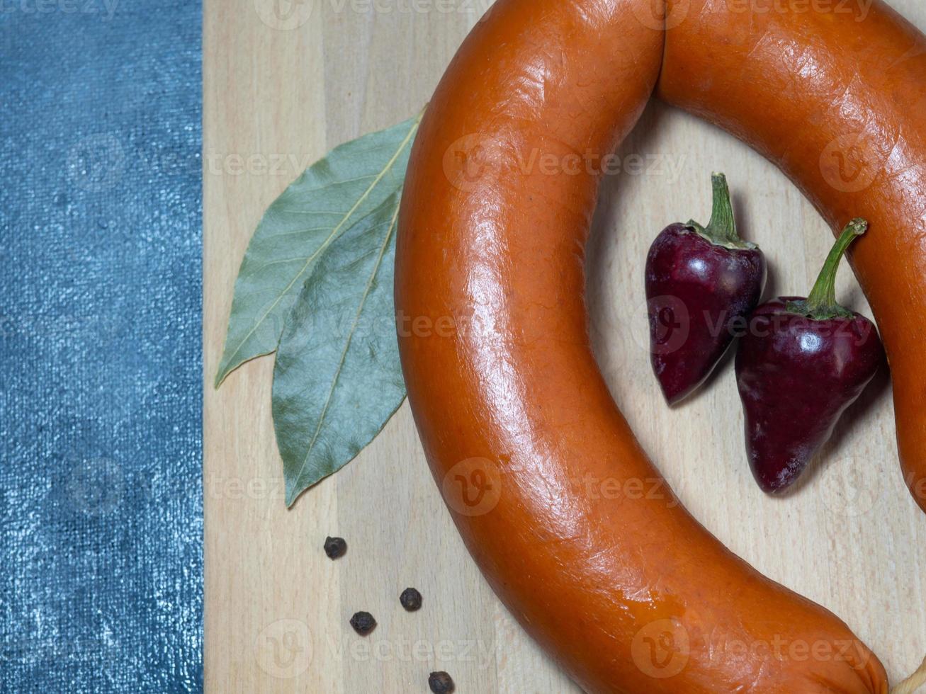 la saucisse se trouve sur une planche de cuisine avec des grains de poivre noir, des piments et des feuilles de laurier. photo