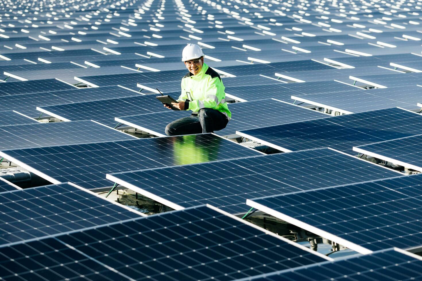 portrait d'un travailleur souriant, installant des batteries solaires, qui se tient sur une échelle à la centrale solaire contre le ciel bleu, montrant le pouce vers le haut. concept de sources d'énergie alternatives. photo