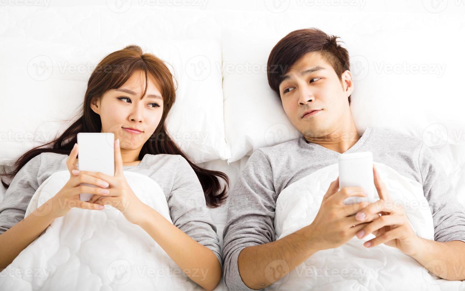 heureux jeune couple dans un lit avec des téléphones intelligents photo