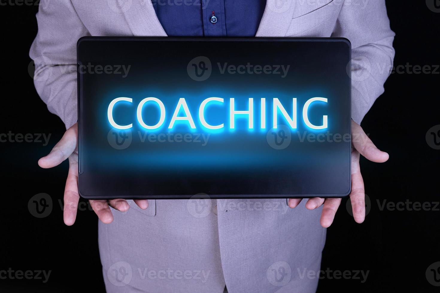 texte de coaching, mot écrit en lettres de néon sur un ordinateur portable noir, devant un homme d'affaires en costume gris. photo