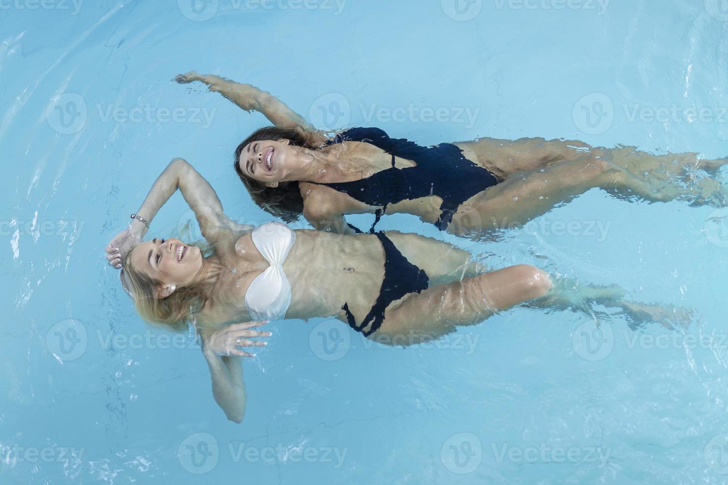 les jeunes femmes se détendent et s'amusent au bord de la piscine du spa de santé. ils flottent sur l'eau dans la piscine, portent un bikini et sont beaux, sereins et insouciants. photo