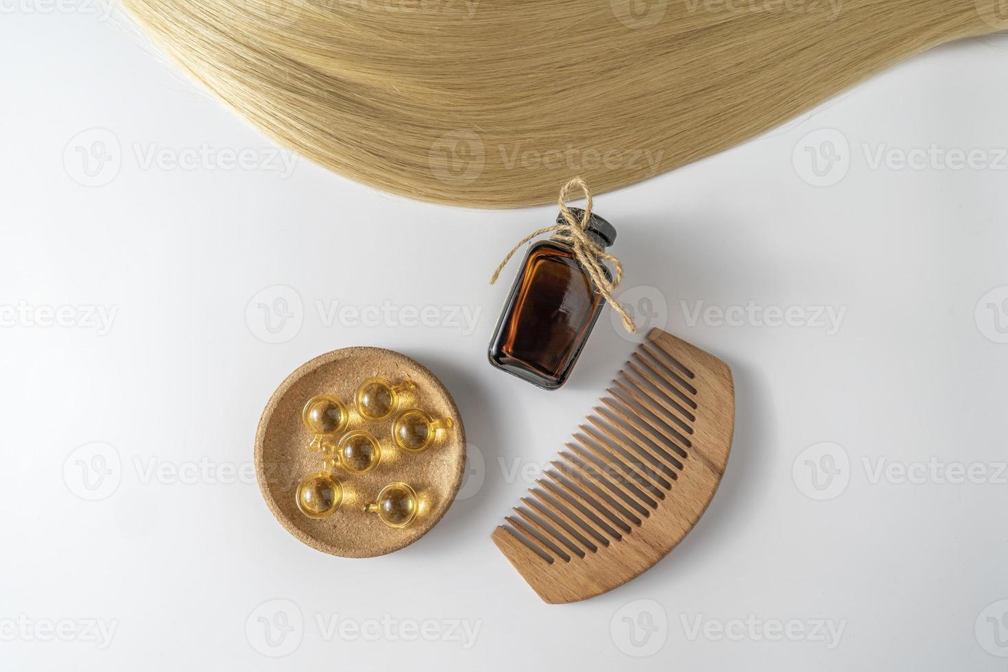 une huile ou un sérum de soin des cheveux dans un flacon compte-gouttes marron et des capsules dorées et un peigne à cheveux en bois posé sur fond blanc, maquette de marketing produit photo