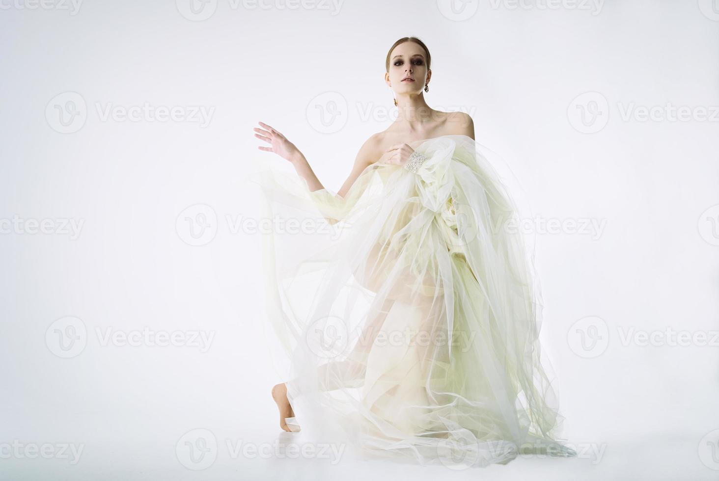 modèle de jeune fille dans un studio photo dans une robe de mariée assise sur un genou jouant avec une robe