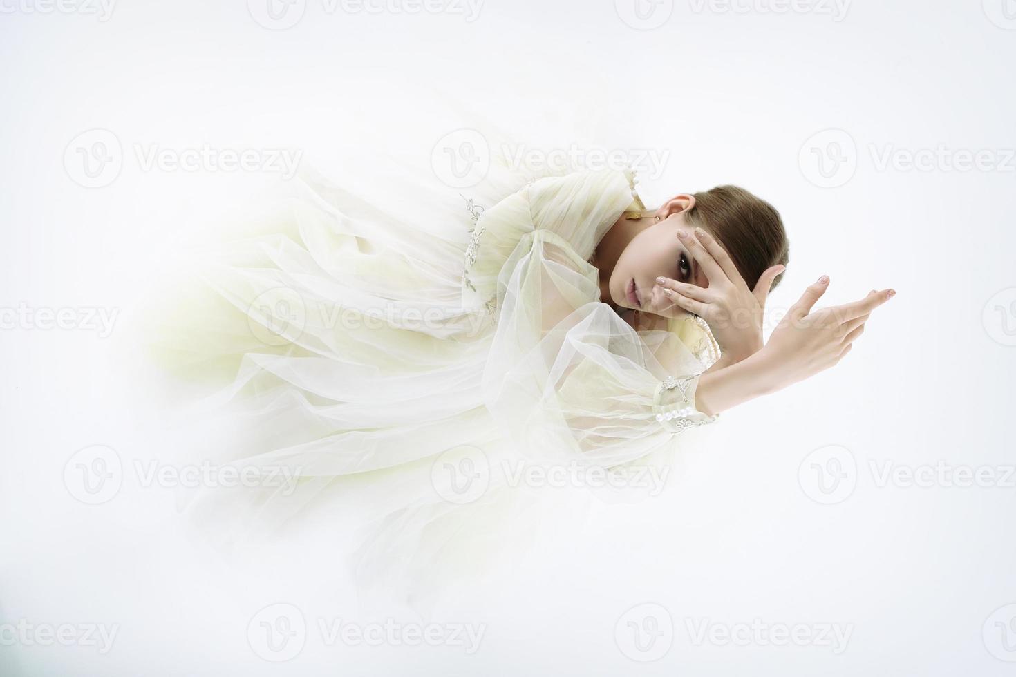 modèle de jeune fille dans un studio photo dans une robe de mariée est agenouillée avec ses bras levés et regardant à travers ses doigts