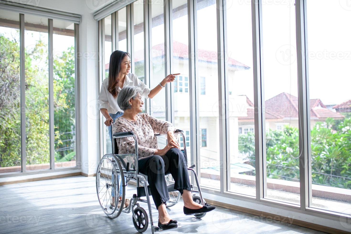 belle fille asiatique aide et prend soin d'une femme âgée âgée assise sur un fauteuil roulant dans le salon de la maison, concept de patient de thérapie senior à la maison. photo