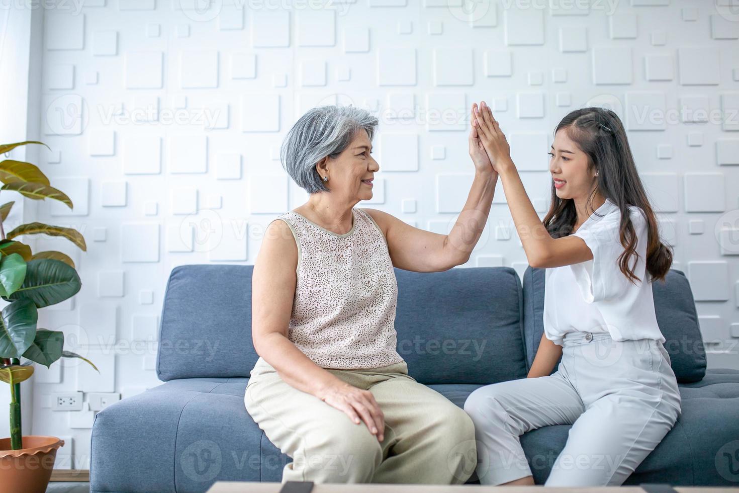 grand-mère et petite-fille asiatiques parlant et salut-cinq à la maison. senior et jeune femme souriante et bonne humeur sur le canapé dans le salon. photo