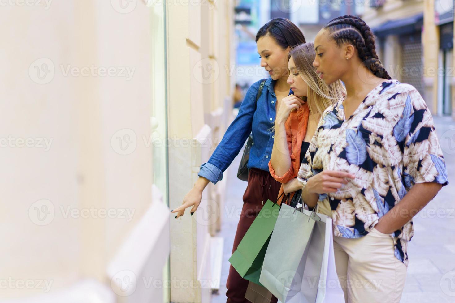 jeunes femmes multiethniques debout dans la rue près de la fenêtre de la boutique de mode photo