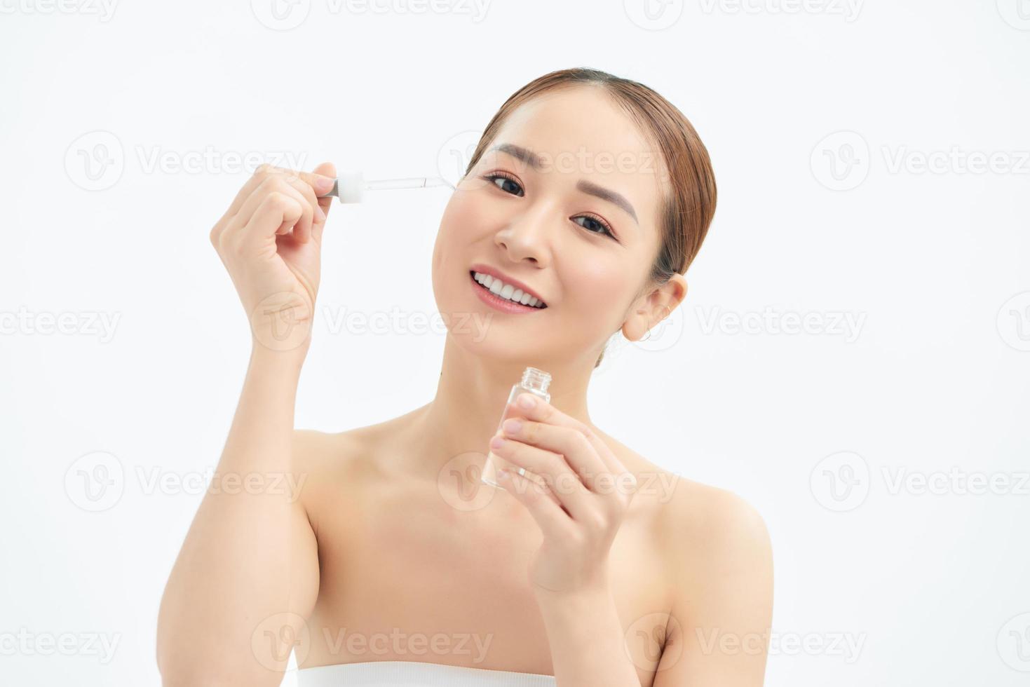 gros plan jeune femme asiatique appliquant du sérum sur son visage. maquillage doux et fond blanc isolé. photo