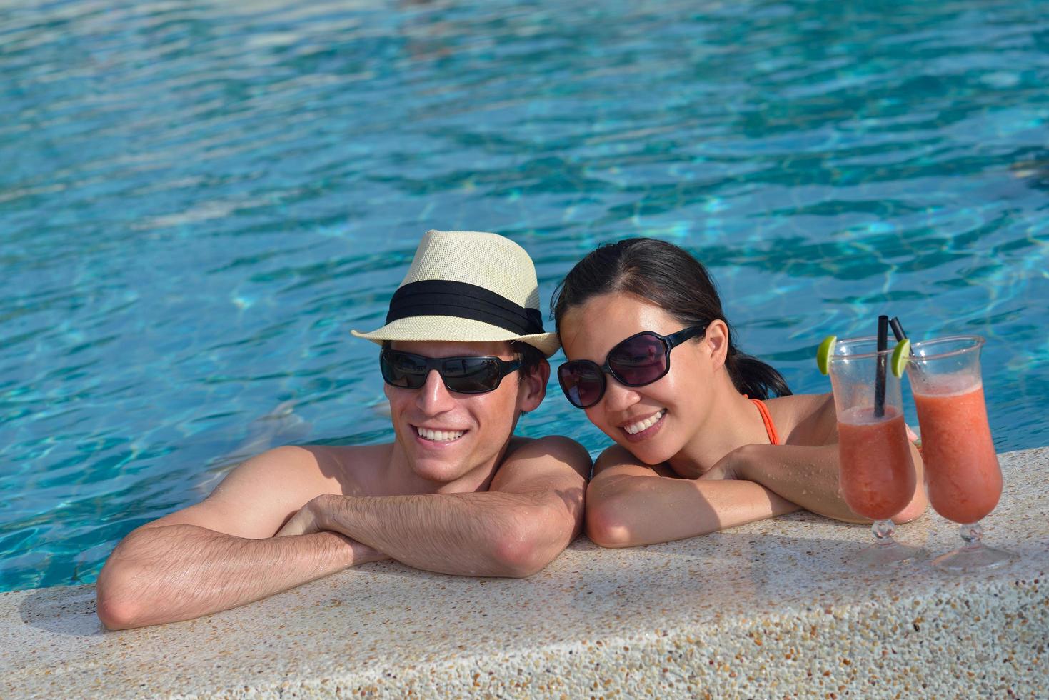 un jeune couple heureux se détend et prend une boisson fraîche au bord de la piscine photo