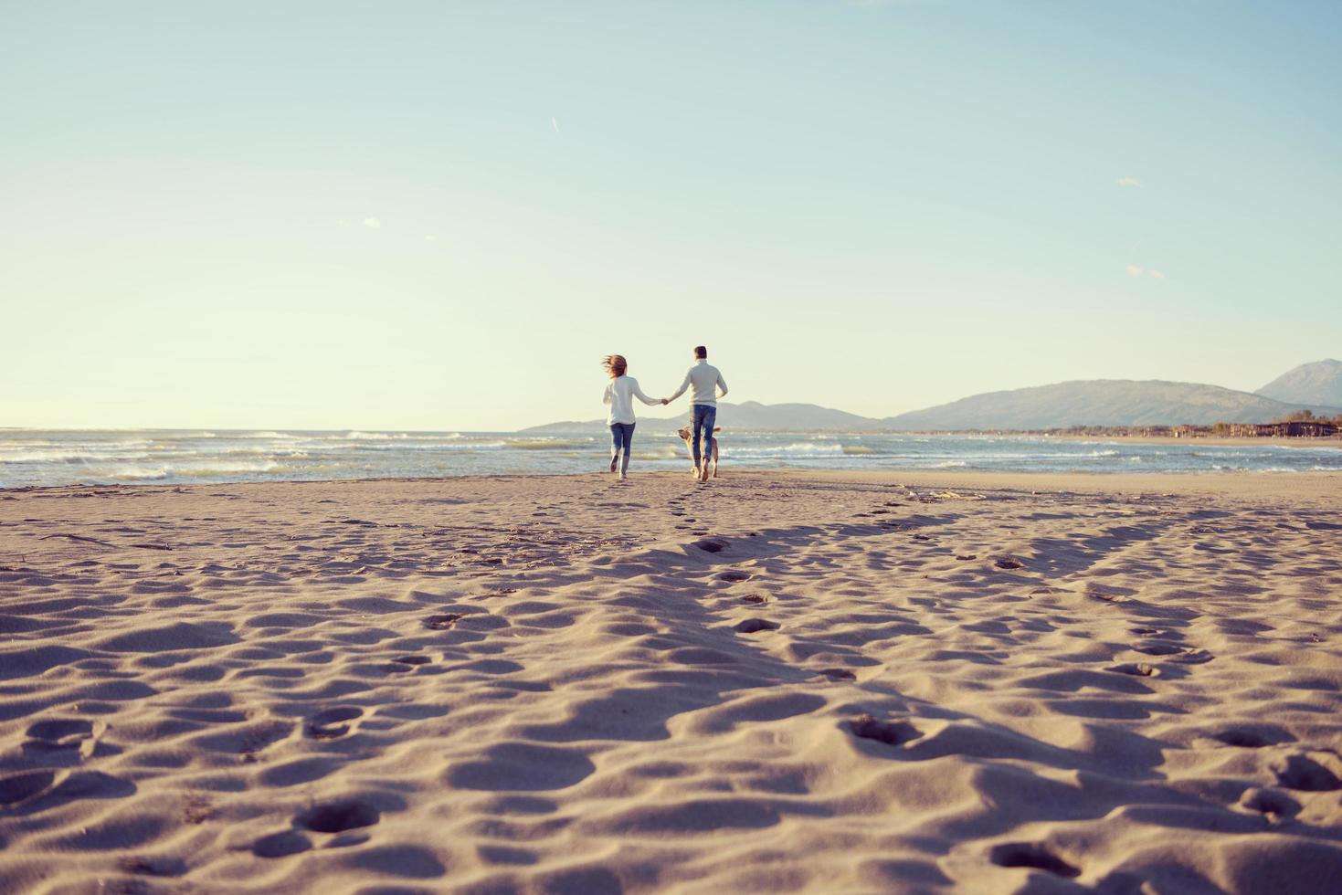 couple avec chien s'amusant sur la plage le jour de l'automne photo