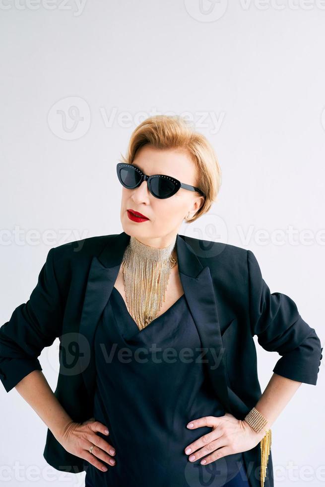 femme mûre à la mode en smoking et lunettes de soleil. maquillage, mode, concept anti-âge photo