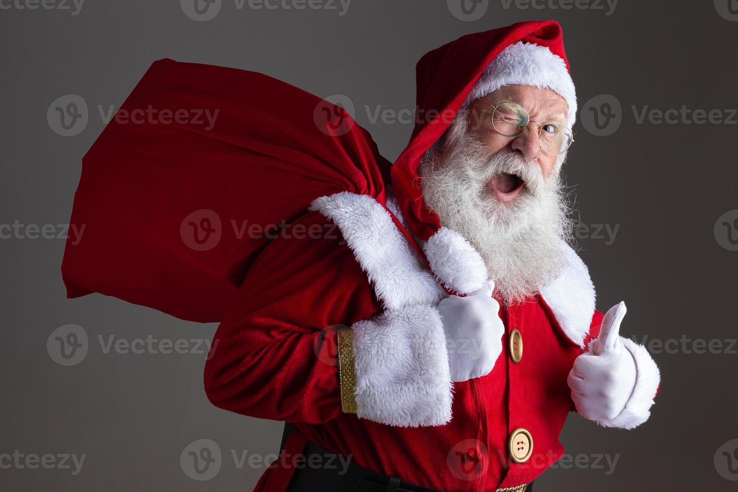 le père noël à lunettes regarde la caméra et sourit, sur fond gris photo