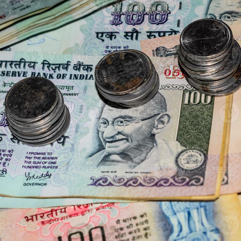 rares vieilles pièces de roupie de banque indienne tombant sur des billets de banque, tombant sur une pièce de monnaie de roupie indienne sur des billets de cent roupies, pièces de monnaie indienne tombant photo