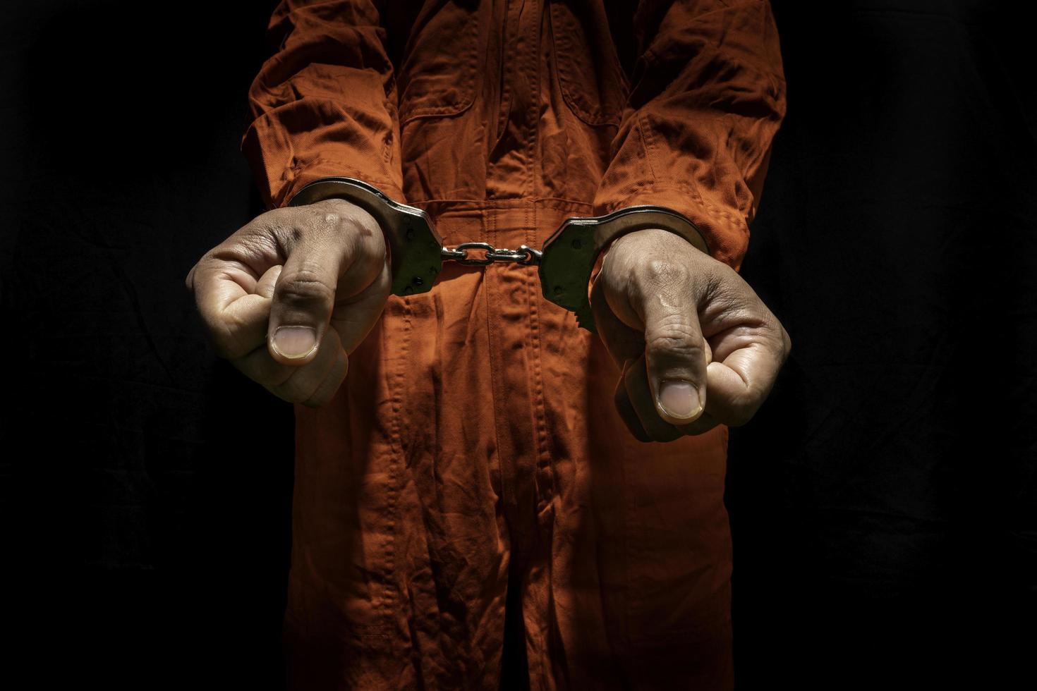 menottes sur un criminel accusé en combinaison de prison orange. délinquant condamné à purger une peine de prison, sur fond noir photo